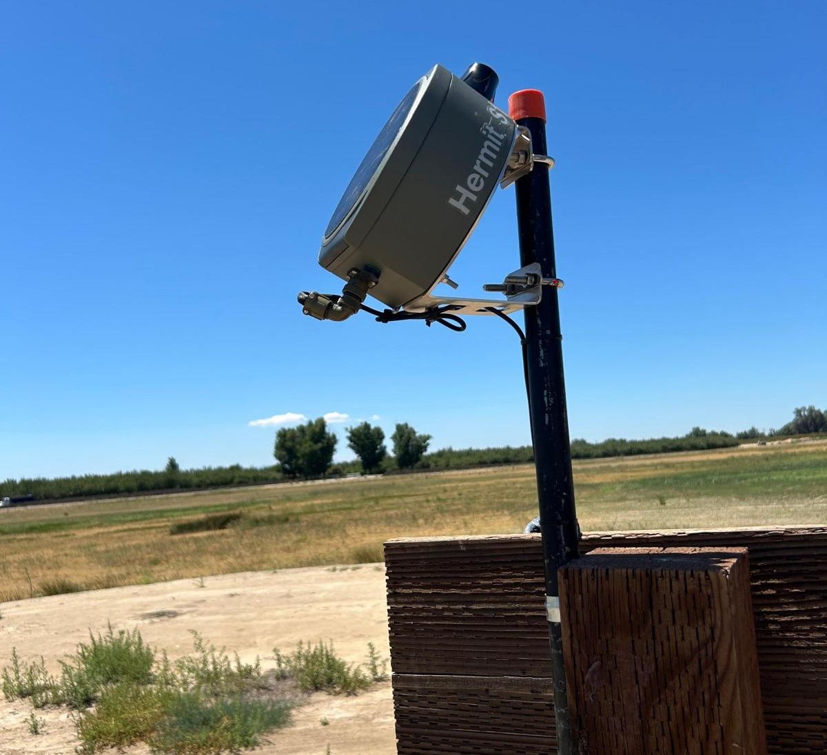 Pole-mounted telemetry unit above a groundwater well housing in an open field