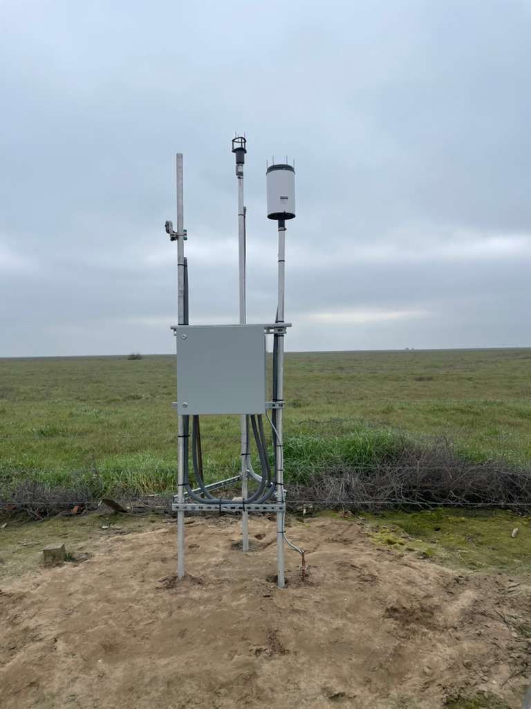 Weather station with rain gauge, sensors and an equipment enclosure in a grassy field
